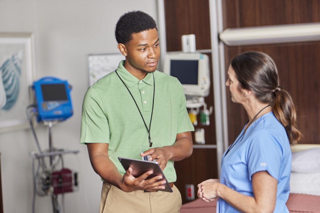 Young male nurse in green scrubs discussing medical information on a tablet with female doctor in blue scrubs